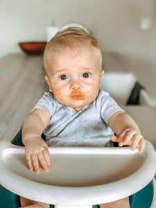 Baby boy in highchair with puree food over his face